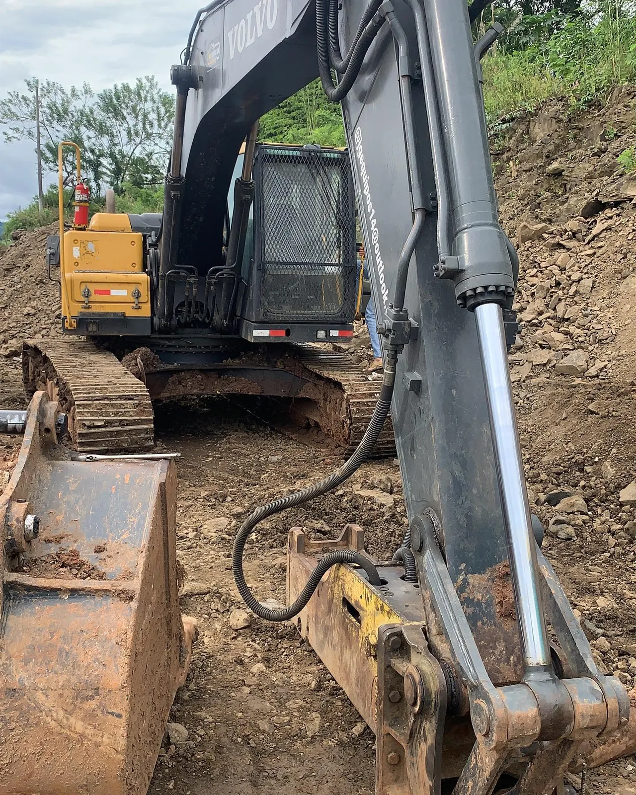Excavadora Volvo con el cucharón y el martillo hidráulico en el suelo, en un talud.