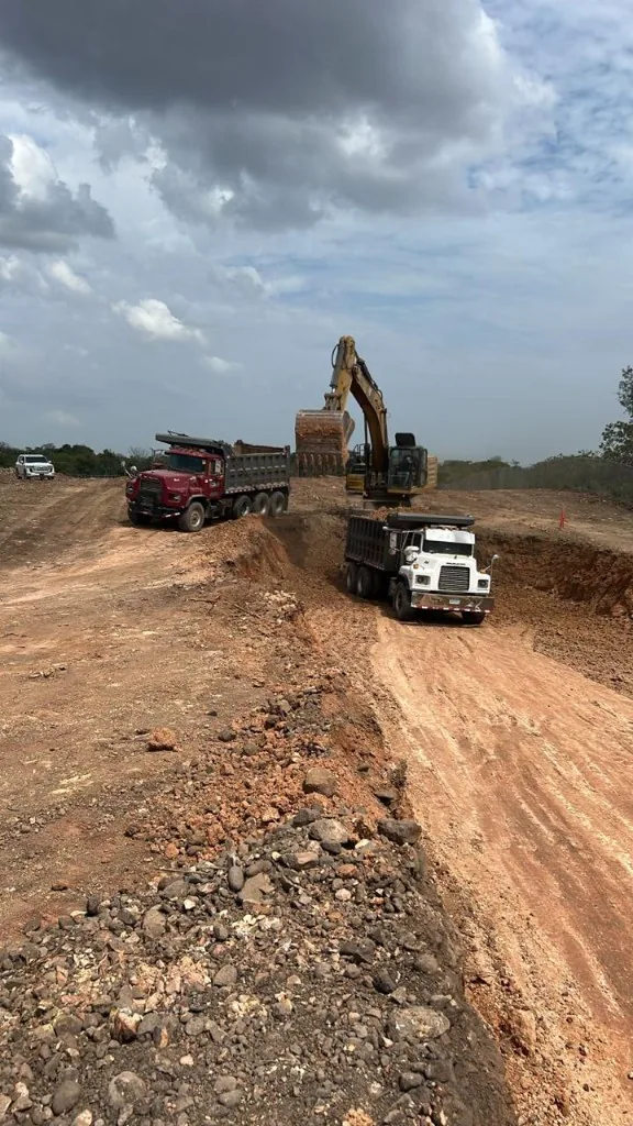 Excavadora y dos volquetes Mack trabajando un corte de tierra.