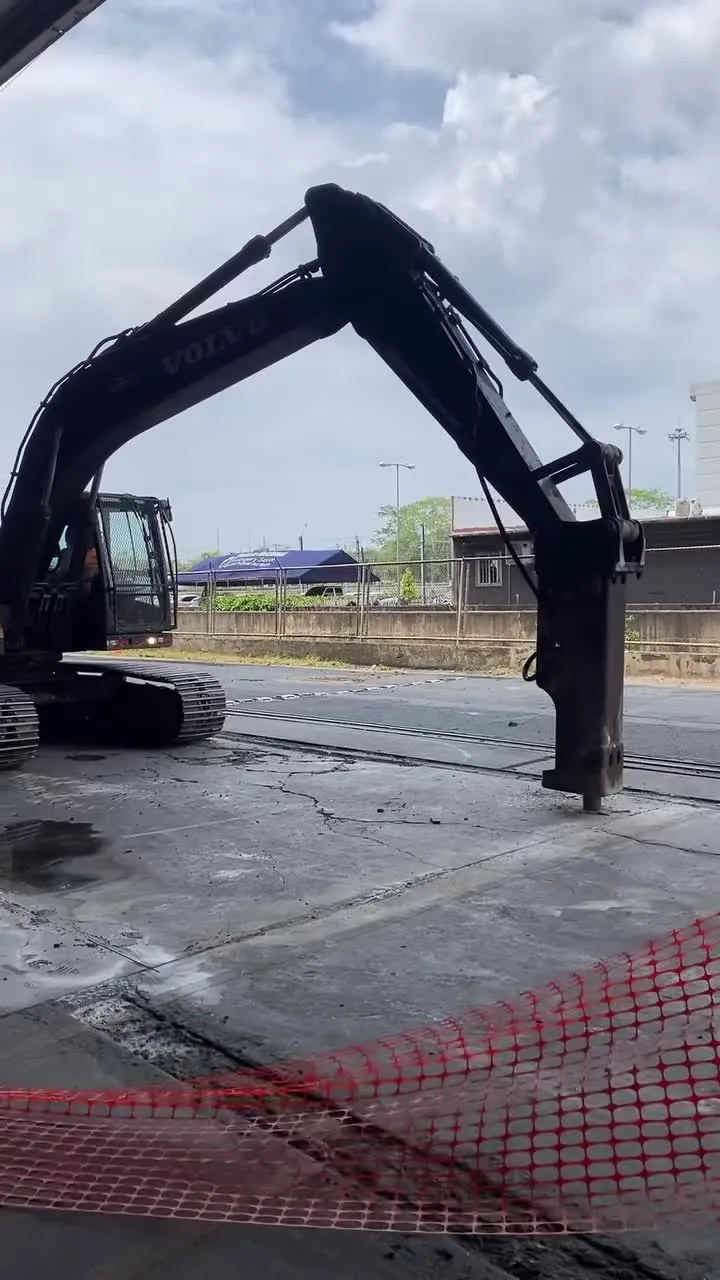 Excavadora Volvo con martillo sobre una losa de concreto, junto a una malla de seguridad.