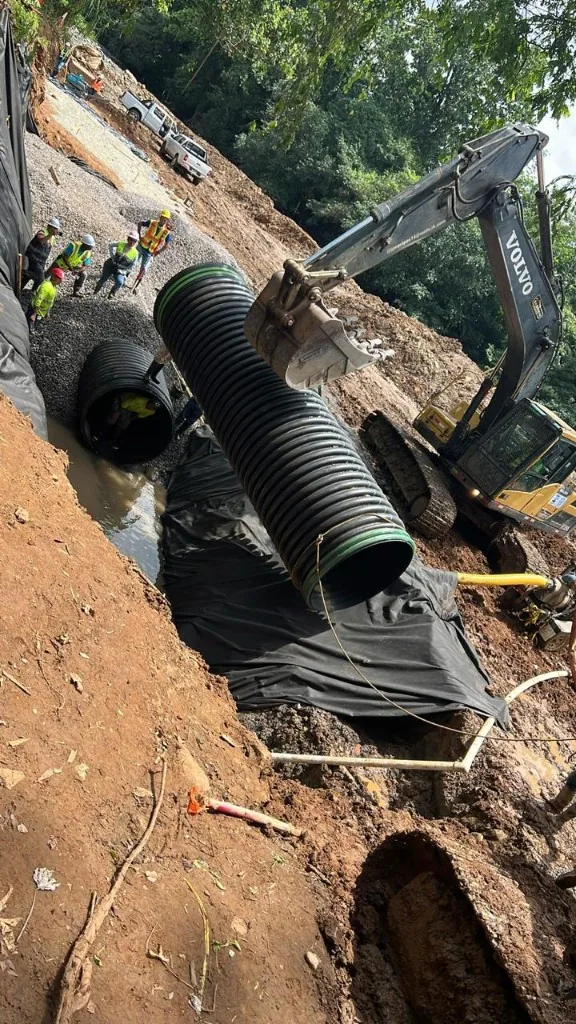 Excavadora Volvo bajando un tramo de tubería sanitaria a la zanja.